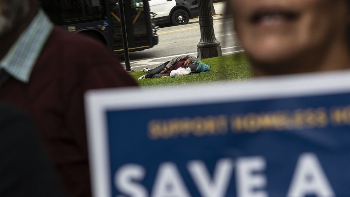 A homeless man sleeps on the lawn at City Hall on Friday during the rally.