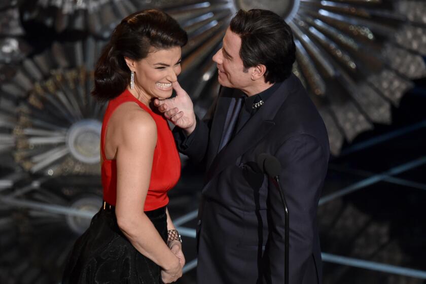 John Travolta holds Idina Menzel's face as they present onstage at the 2015 Oscars