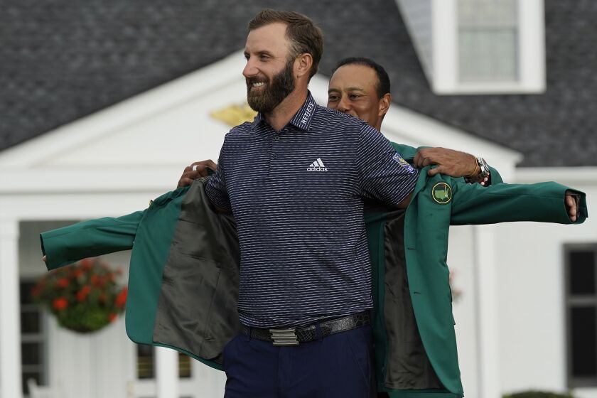 Tiger Woods helps Masters champion Dustin Johnson with his green jacket.
