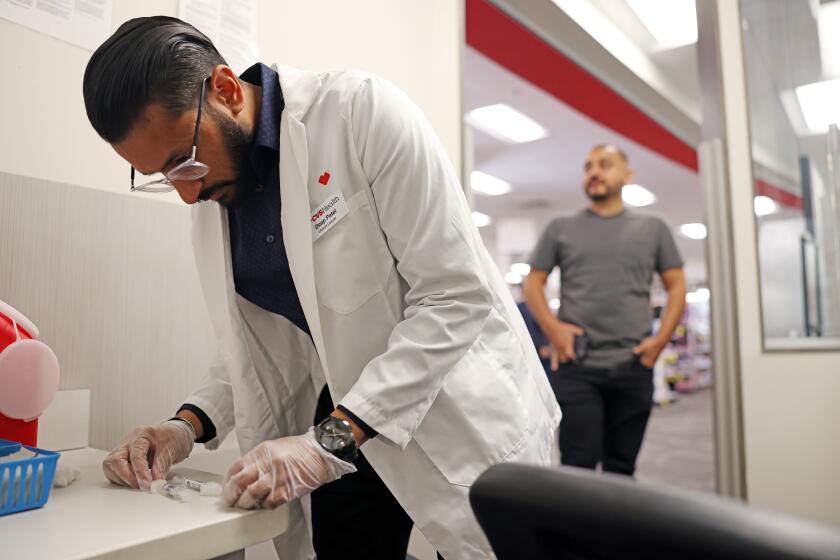 HUNTINGTON PARK-CA-AUGUST 28, 2024: Pharmacist Deep Patel, left, prepares the flu and Covid-19 vaccine for Brandon Guerrero, 34, of Compton, right, at CVS in Huntington Park on August 28, 2024. (Christina House / Los Angeles Times)