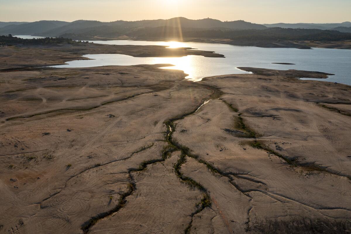 Sun reflects off water in a cracked and dry lakebed.