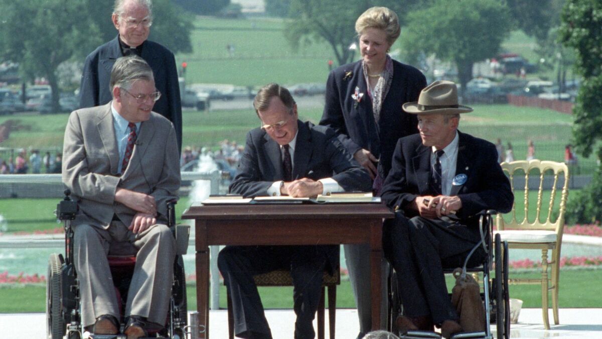President George H. W. Bush, center, signs the Americans with Disabilities Act during a ceremony on the South Lawn of the White House on July 26, 1990. The act has been cited in an increasing number of lawsuits against businesses over the accessibility of their websites.