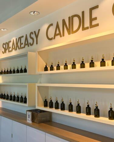 Speakeasy Candle Co. with brown jars displayed on cream-colored shelves.