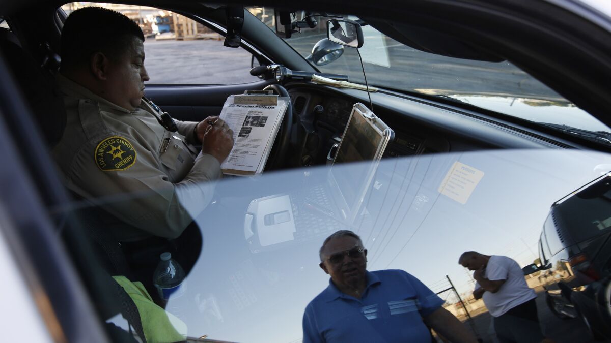 L.A. County Sheriff's Deputy Ivan Davanzo fills out a report after a burglary call from James Oakes, seen reflected in the window, in the City of Industry.