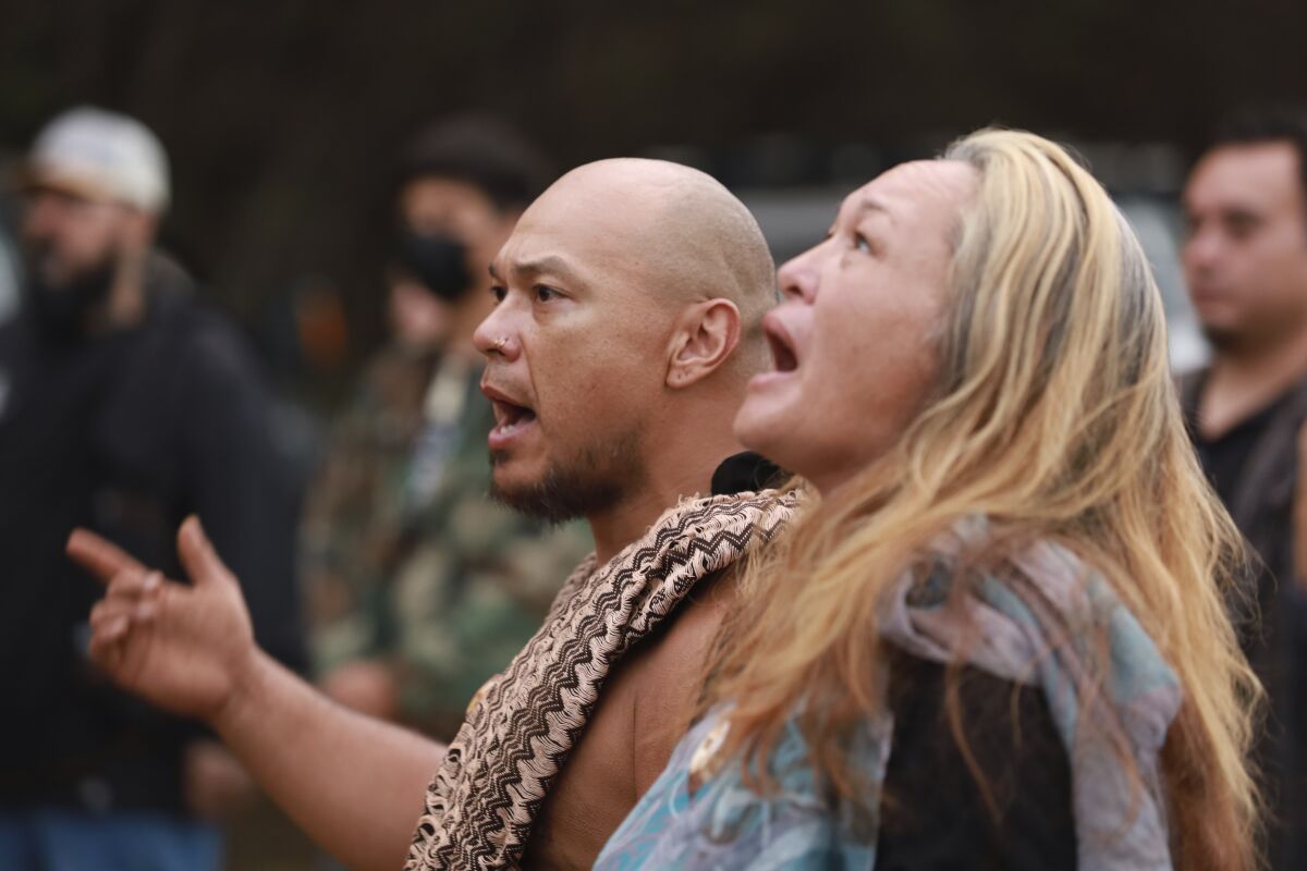 In this photo provided by Bradford Nakamura, Makaio Villanueva, left, and Gina Peterson chant about the importance of water during a traditional Hawaiian ceremony on December 12, 2021, in Honolulu. Protesters who erected the shrine at the gates of the headquarters of the commander of the U.S. Pacific Fleet oppose the U.S. Navy's use of a giant fuel storage tank facility because jet fuel leaked into a drinking water well. (Bradford Nakamura via AP)