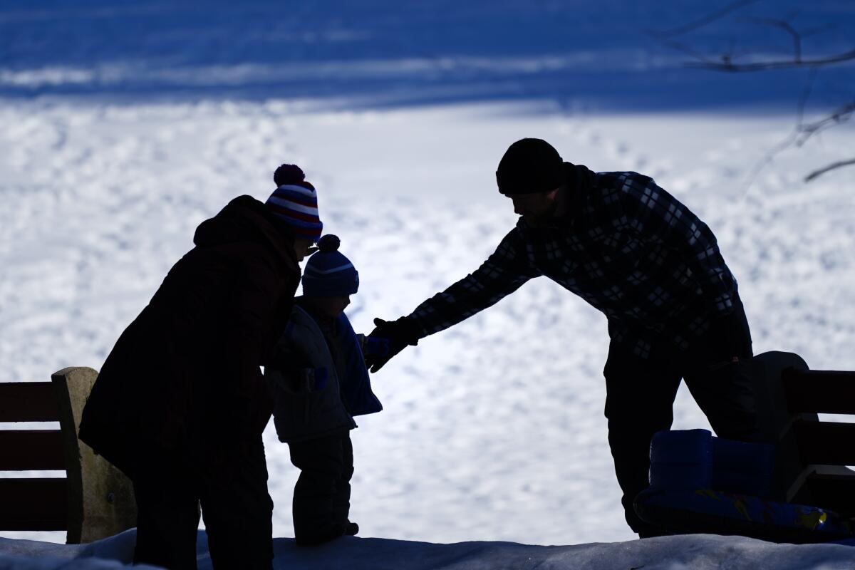 FILE - In this Feb. 5, 2021 file photo, a couple helps a child on a snow covered embankment at in Huntingdon Valley, Pa. The cost to adopt a child can range from $20,000 to $45,000, according to the Child Welfare Information Gateway. Each year, millions of families navigate the expense and a process that can be overwhelming for prospective adoptive parents who aren’t familiar with the steps or fees involved. (AP Photo/Matt Rourke)