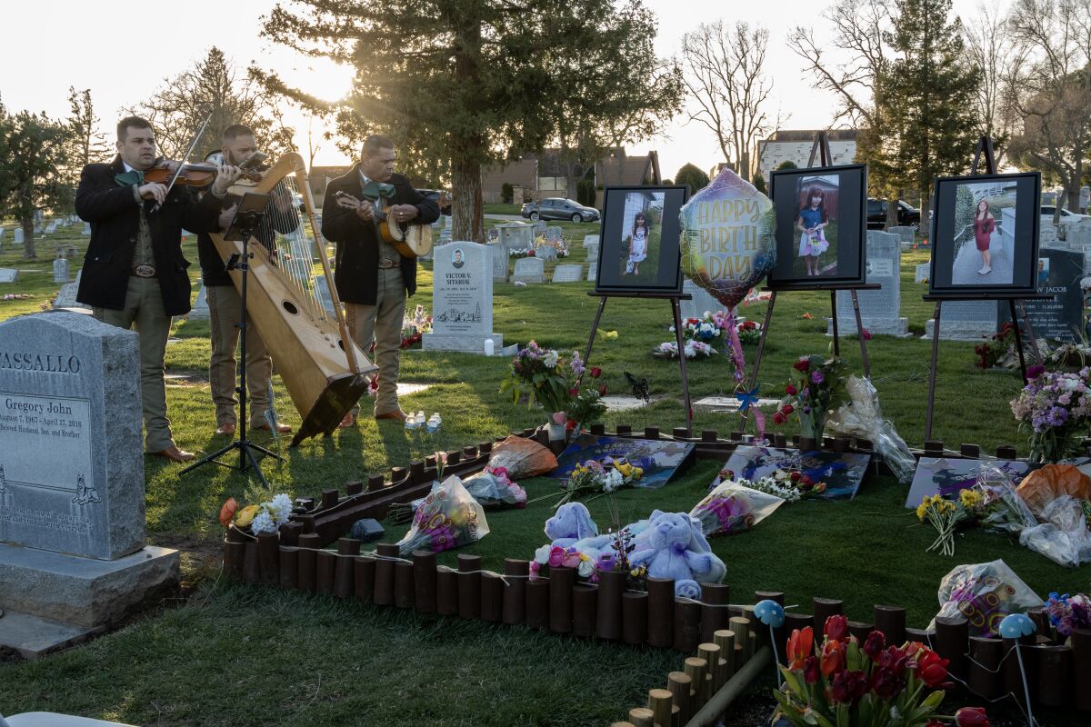 A mariachi trio performs at a cemetery, next to three graves with photos and flowers