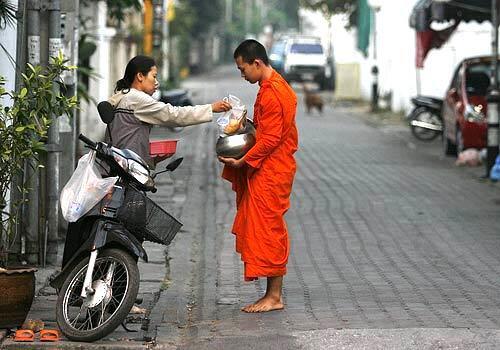 A woman offers food to a monk in the early morning hours in Chiang Mai, Thailand.