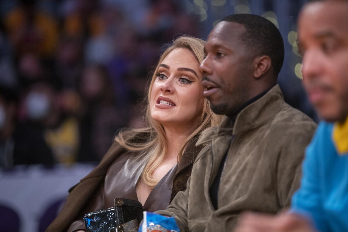 Adele in a brown top and blazer sitting next to Rich Paul in a brown jacket at a basketball game