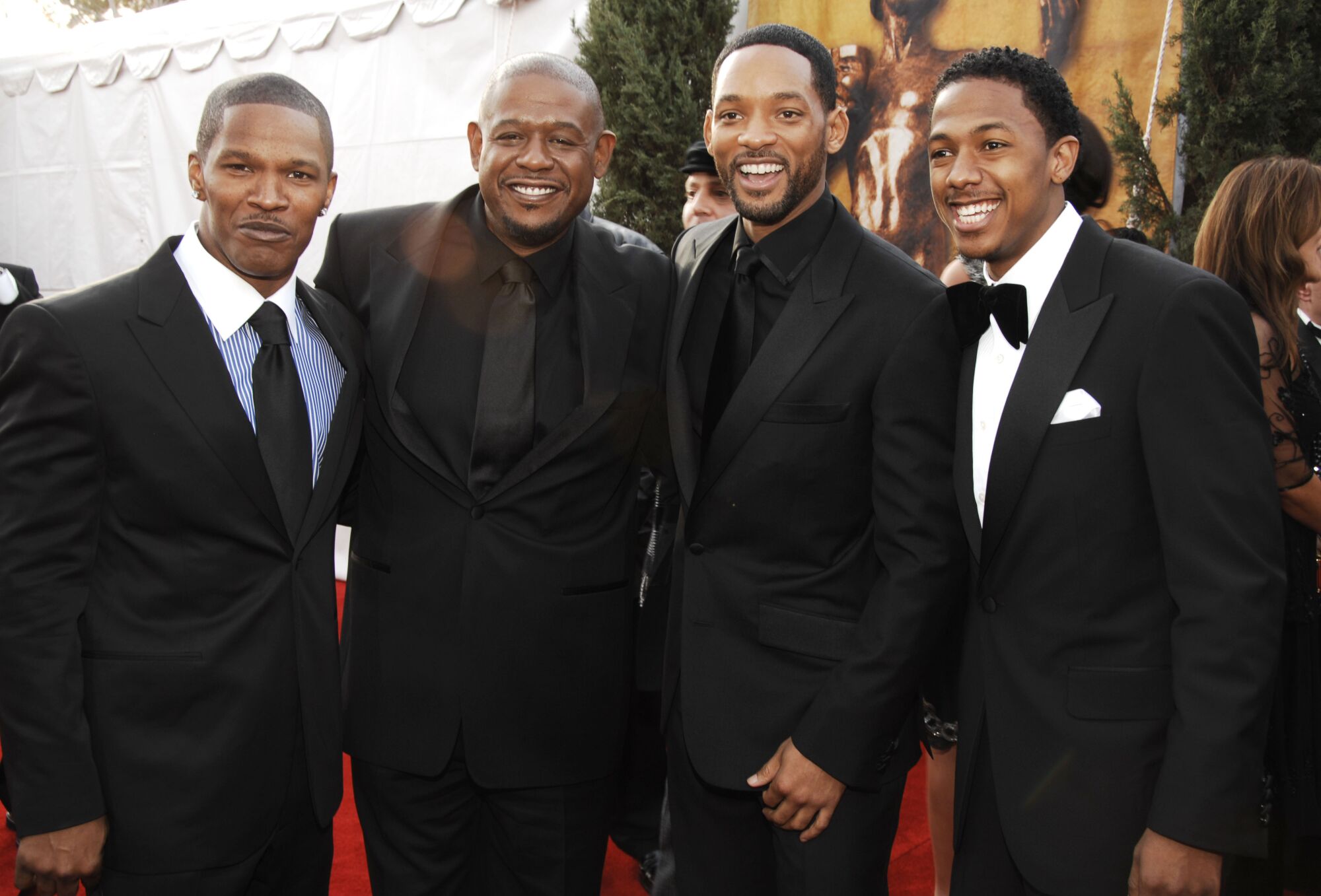 Four men outfitted in suits and tuxedos pose on the red carpet at an award show