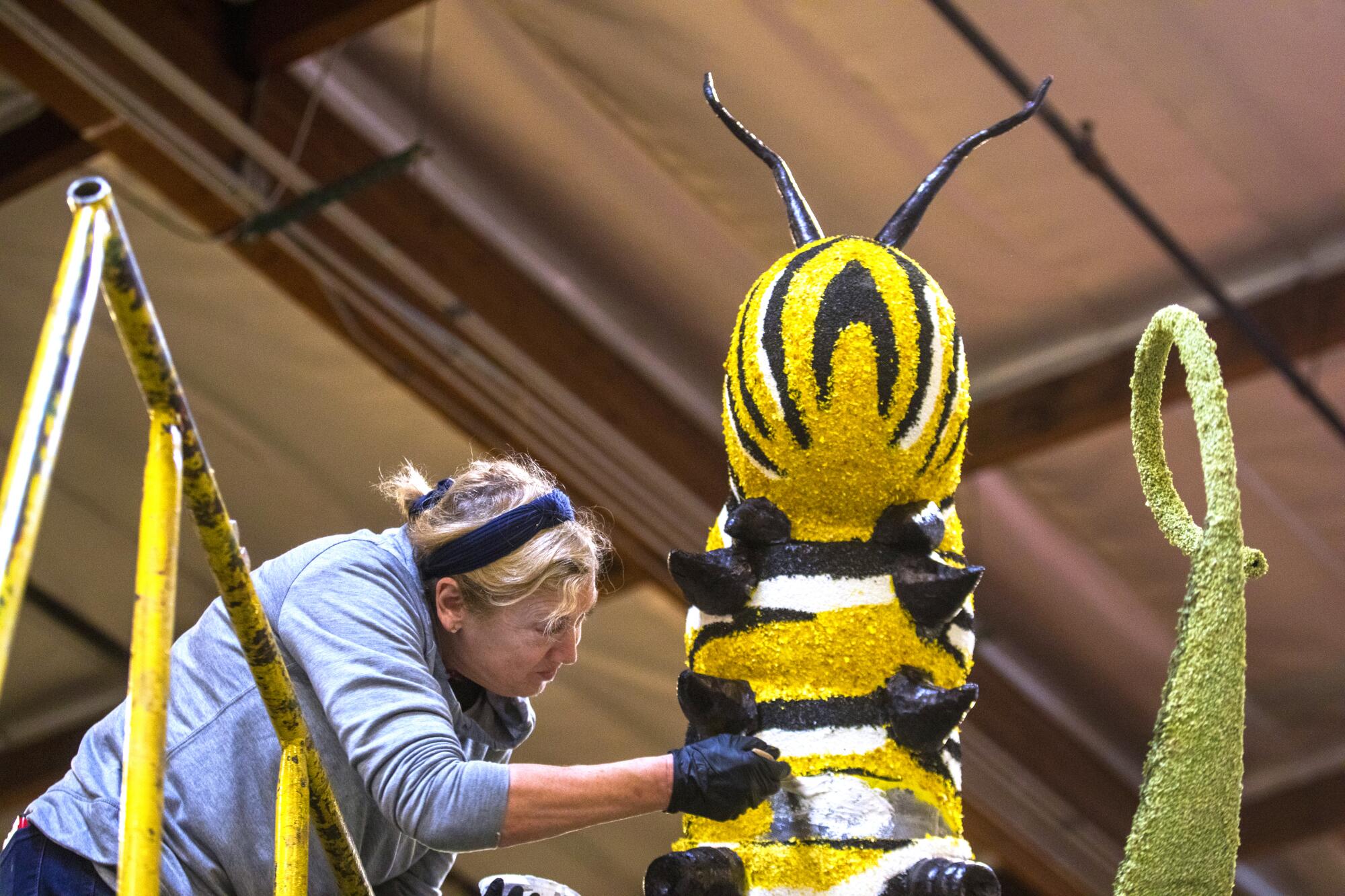 A woman works on a floral-covered bumble bee for a float