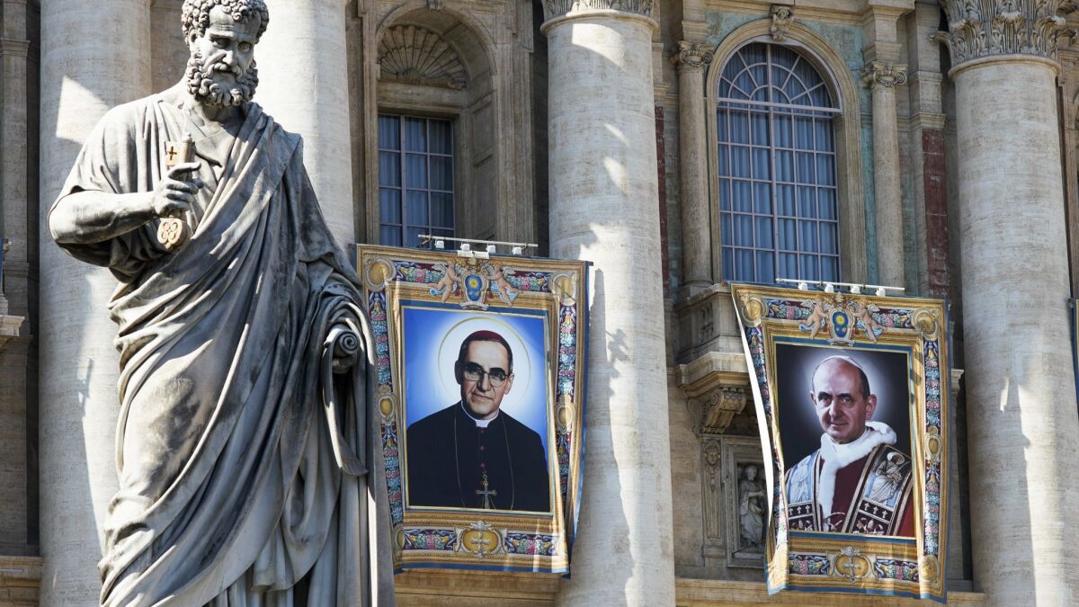 Tapestries depicting Archbishop Oscar Romero, left, and Pope Paul VI hang from a balcony of the facade of St. Peter's Basilica at the Vatican on Saturday.