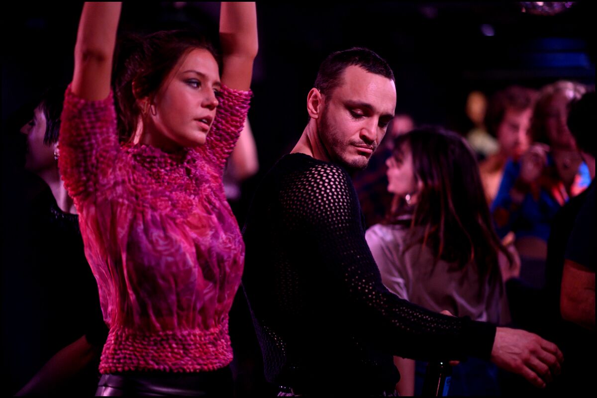 A woman in a purple top and a man dance in a club.