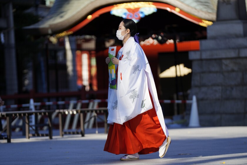 A miko, or shrine maiden, wearing a protective mask to help curb the spread of the coronavirus, walks though the Kanda Myojin shrine Friday, Dec. 3, 2021, in Tokyo. (AP Photo/Eugene Hoshiko)