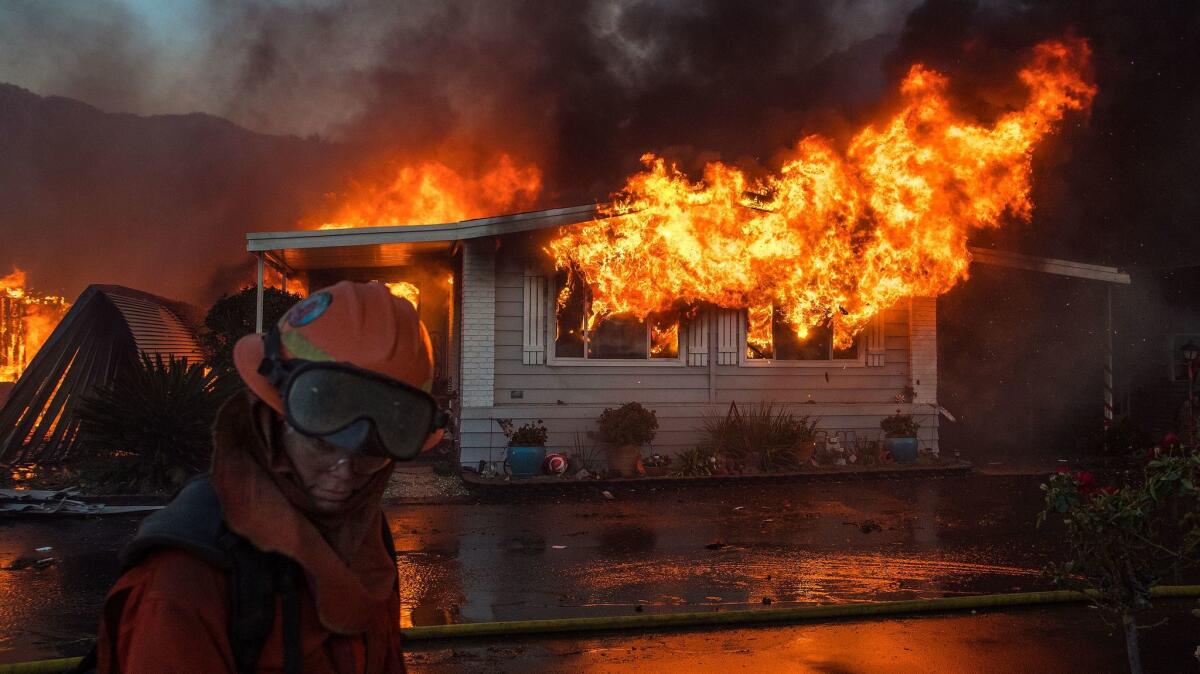 A firefighter turns away from the heat as flames explode through the front windows of a home burning in the Lilac fire in northern San Diego County.
