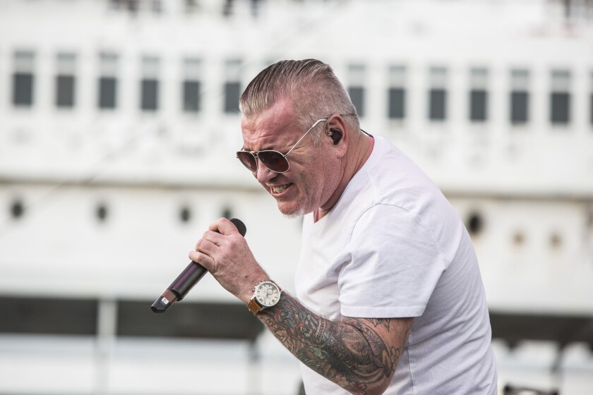A man in a white T-shirt singing into a microphone.