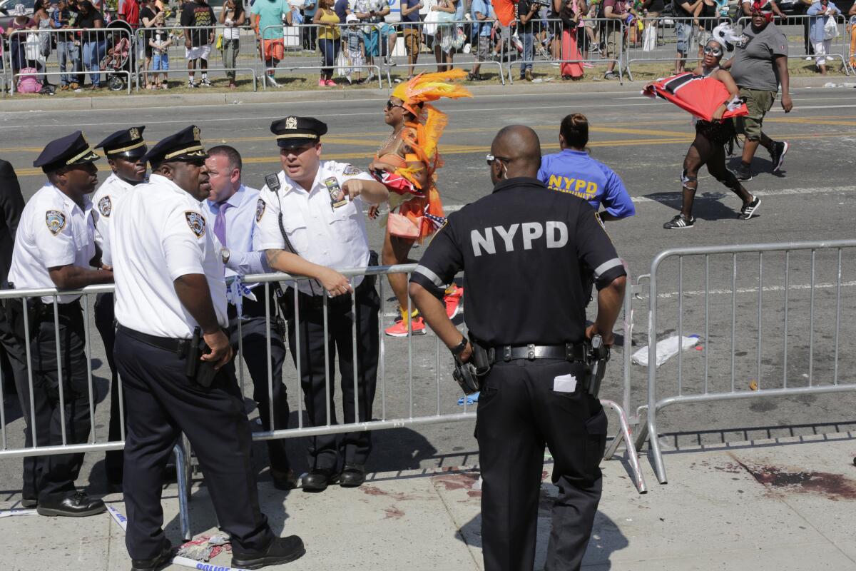 New York City police officers stand on the scene of a fatal stabbing in Brooklyn on Sept. 7 as participants in the West Indian Day Parade pass behind them.