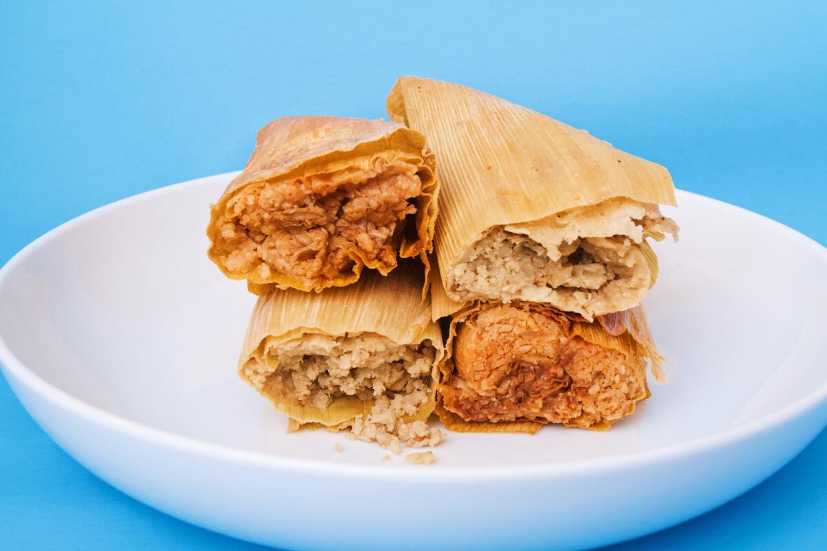 A stack of four Cena Vegan tamales stacked, two on two, in a white bowl against a blue background