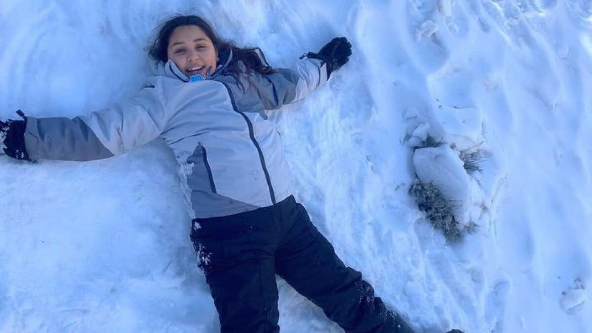 A young girl smiles while lying in the snow