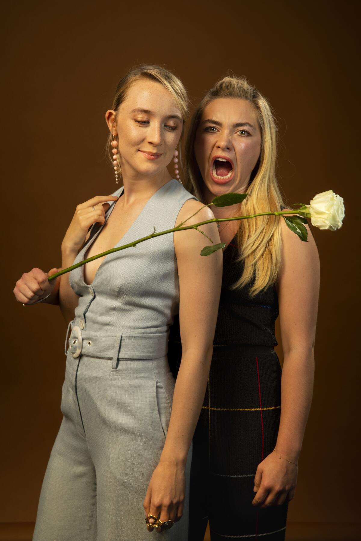 Florence Pugh, right, stands slightly beside and behind Saoirse Ronan, holding a long-stemmed white rose in front of them.