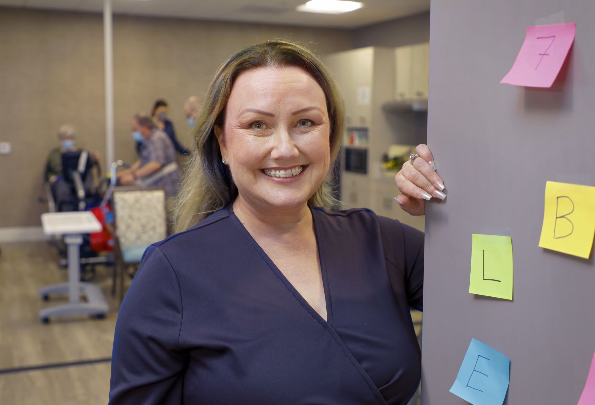 a woman stands next to a gray board with post-it notes on it 