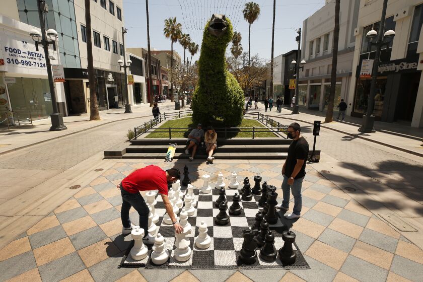 SANTA MONICA, CA - MAY 04: Jeremy Canchola, left, visiting from Ohio plays chess with his uncle Alex Rodriguez on the Third Street Promenade in Santa Monica on Tuesday May 4, 2021 as Los Angeles County continues to rebound dramatically from a deadly winter COVID-19 surge, and with vaccinations continuing at a rapid pace there's increasing certainty that public health officials will move the county (and its many businesses, large and small) into the state's least restrictive reopening tier this week. Third Street Promenade on Tuesday, May 4, 2021 in Santa Monica, CA. (Al Seib / Los Angeles Times).