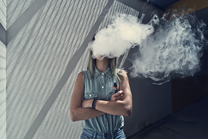 A young woman exhales a cloud of vapor
