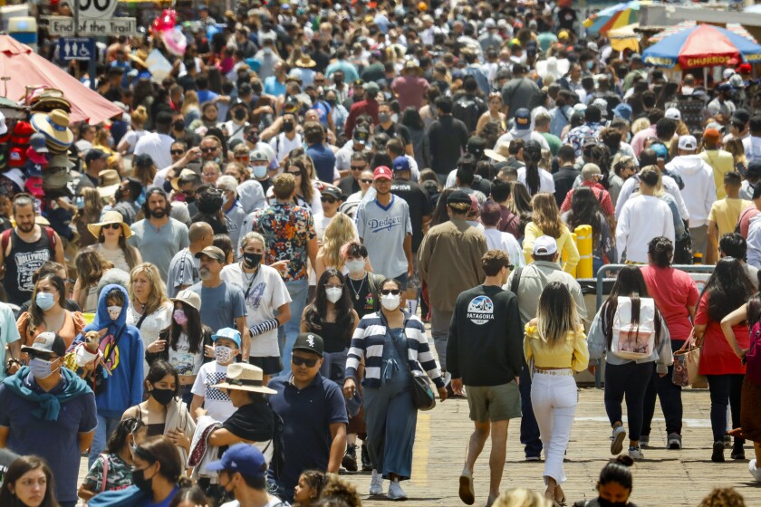 A crowd of people, some with masks, walk in Santa Monica.
