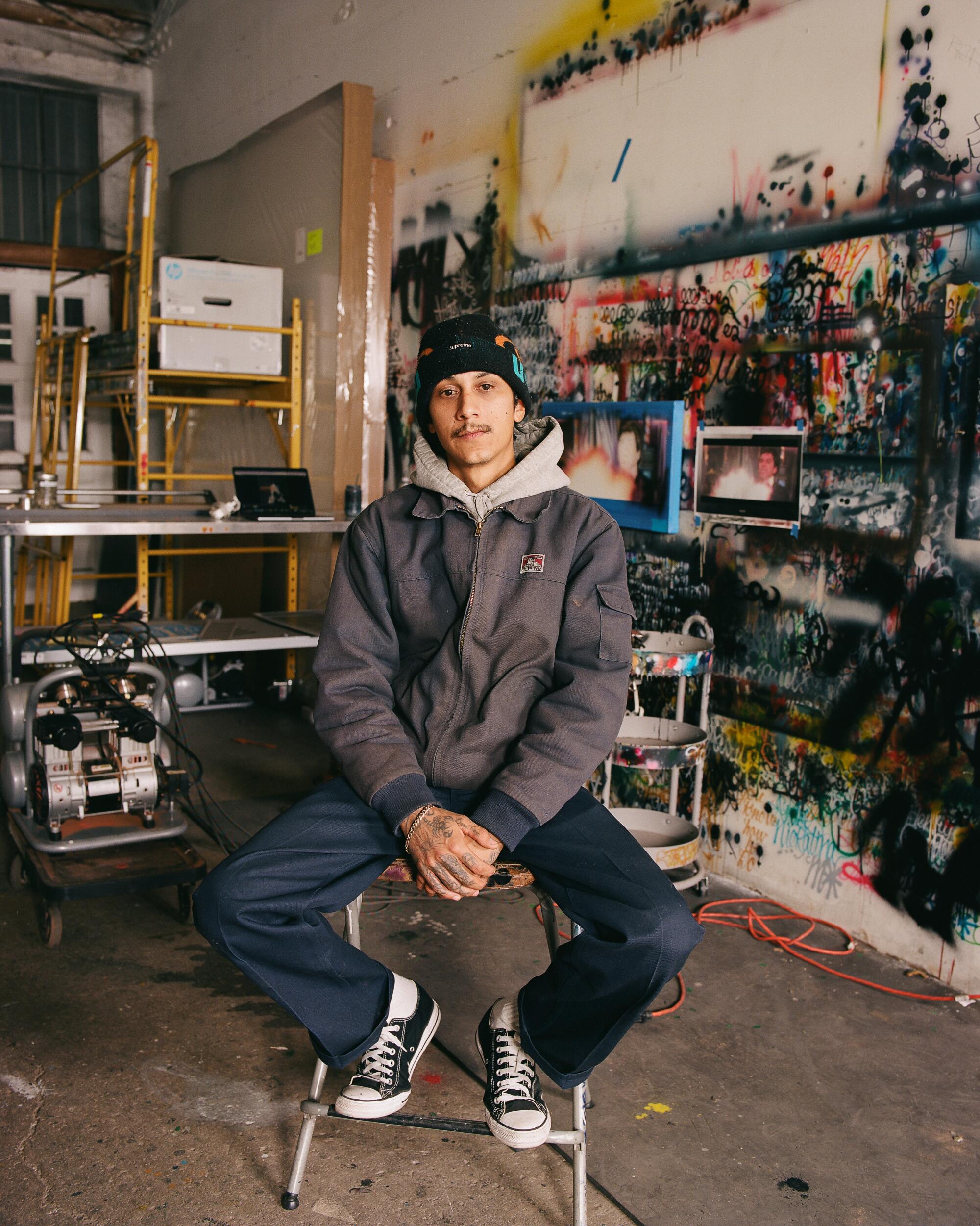 Mario Ayala sits in his spray paint-splattered studio