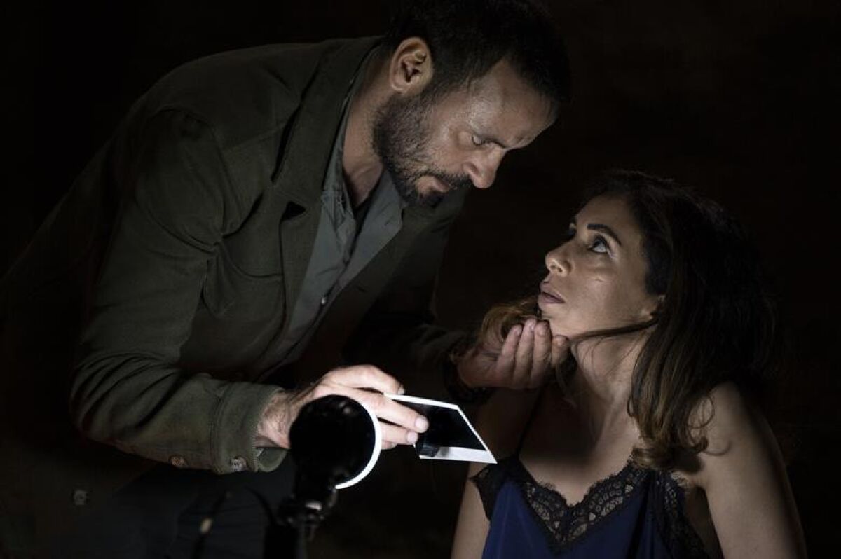 A man tilts a woman's head up to look at a Polaroid photo.