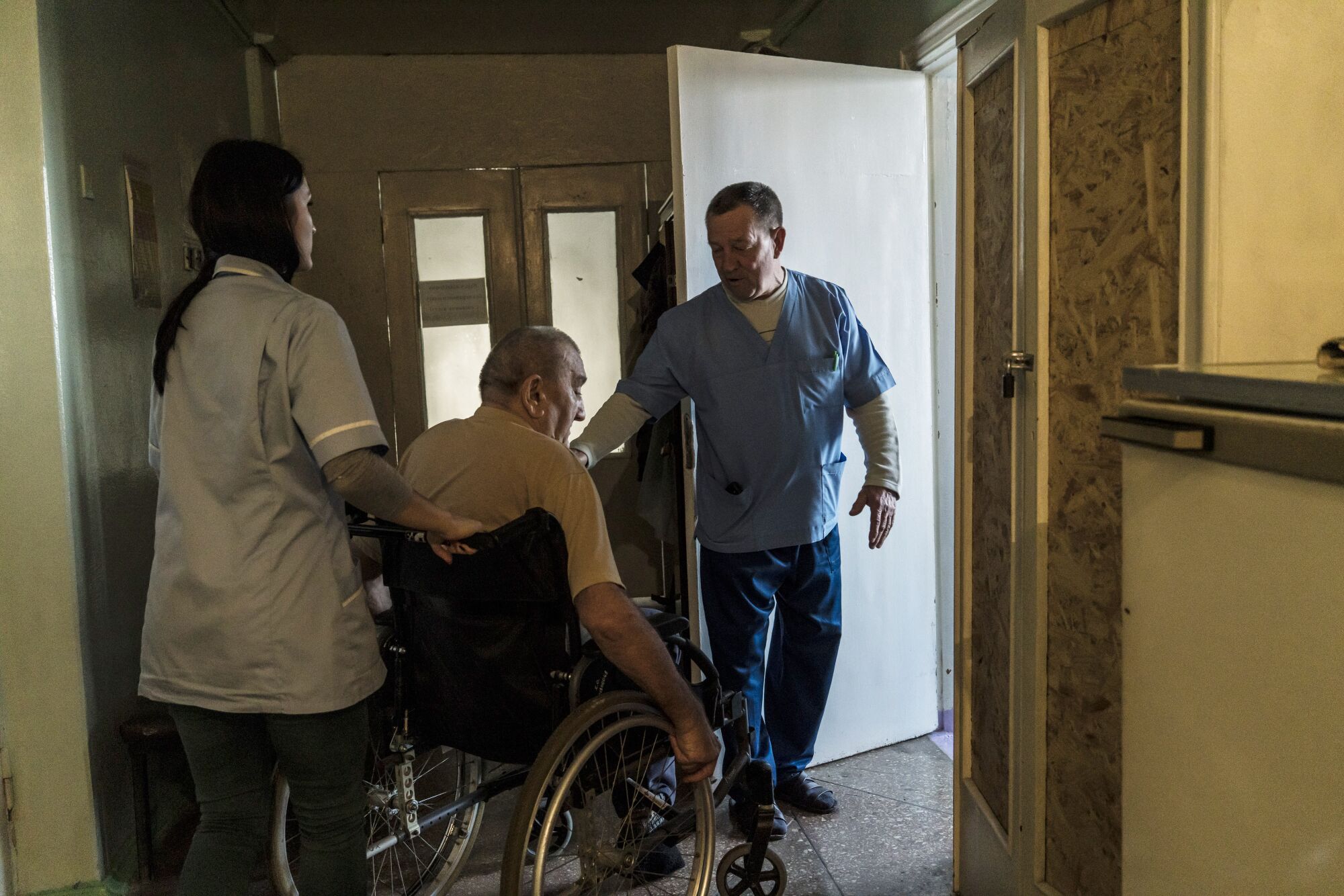 Anatoly Arkatov, the head surgeon, guides a patient in a wheelchair to an examination room at the Avdiivka Central City Hospital.