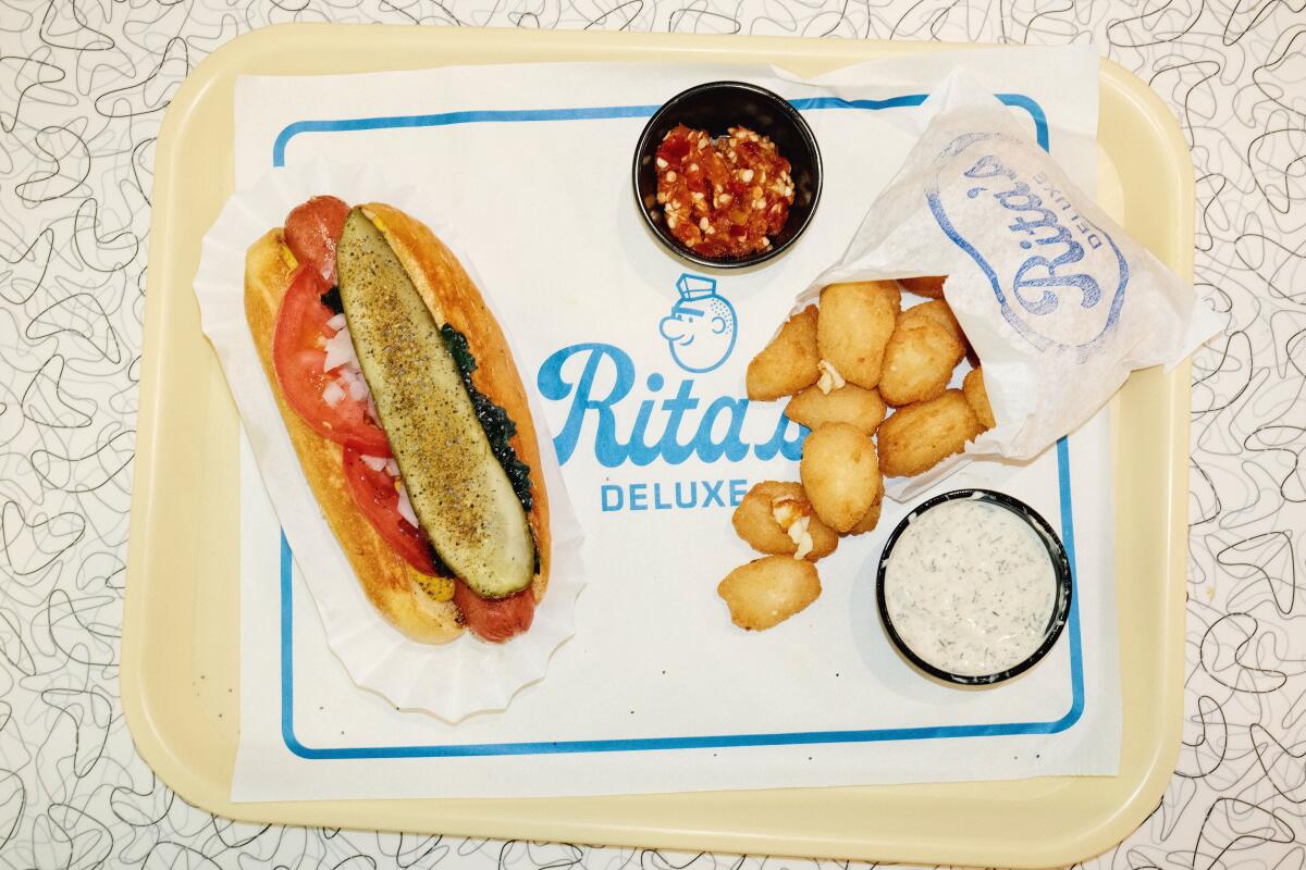 An overhead photo of a Chicago dog with paper bag of beer-battered cheese curds on a yellow tray at Rita's Deluxe in downtown