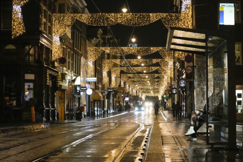 A lone girl waits for a tram in a near-deserted street full of closed restaurants, bars and shop under a partial lockdown in Amsterdam, Netherlands, Friday, Nov. 26, 2021. The Dutch government tightened its lockdown Friday night amid swiftly rising infections and ICU admissions. (AP Photo/Peter Dejong)