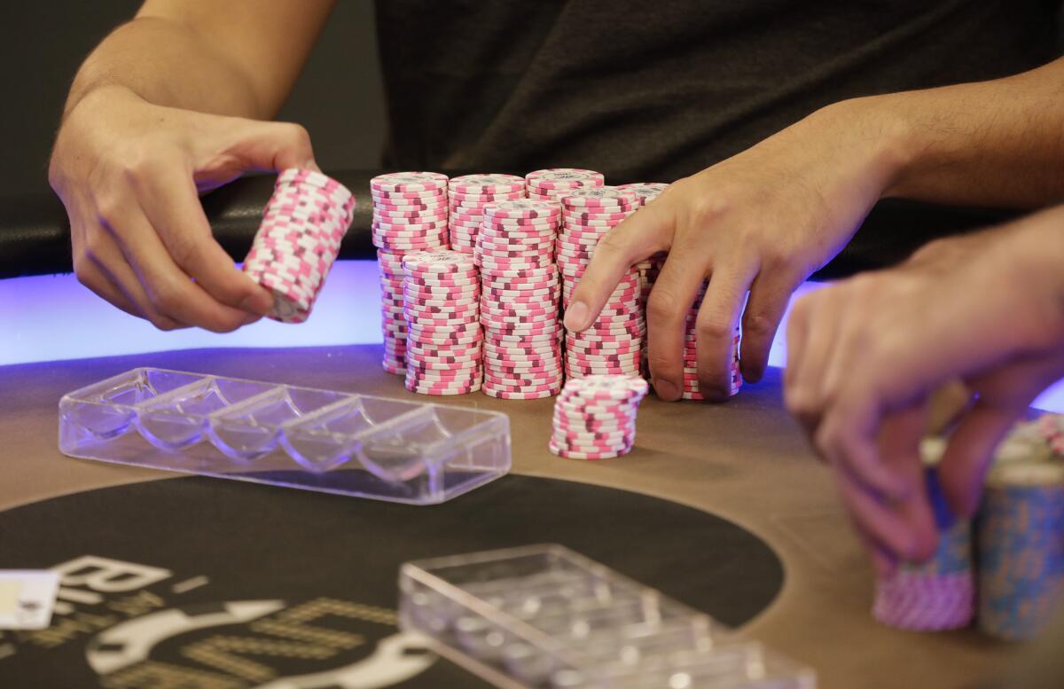 Hands shown stacking pink colored chips at a poker table