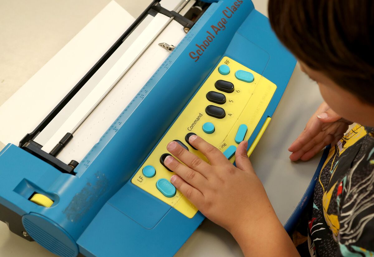 Mason Lopes, 11, of Santa Ana uses his left hand to press down buttons on a Mountbatten Brailler at Beyond Blindness.