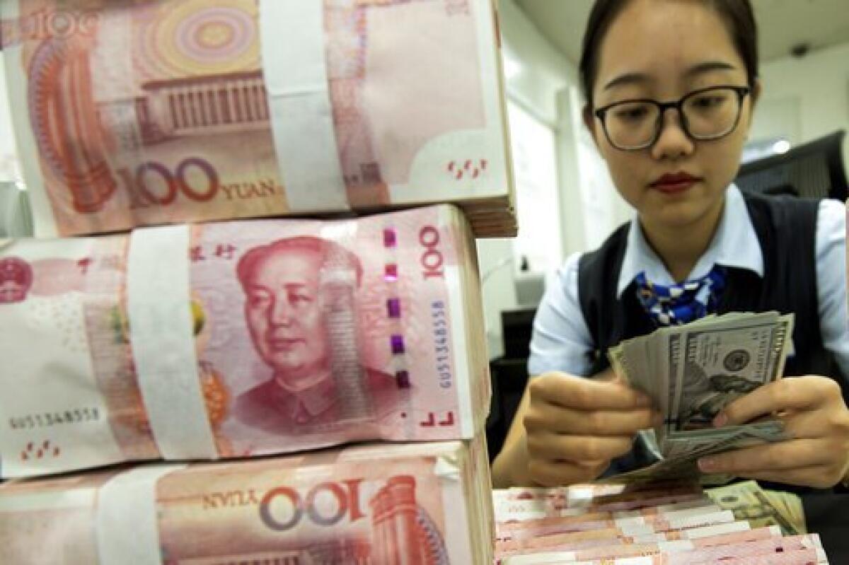 A bank employee counts U.S. dollars next to stacks of Chinese yuan at a bank outlet in Hai'an in eastern China's Jiangsu province.