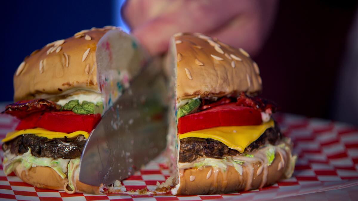 A knife slices through a cake that looks very much like a burger