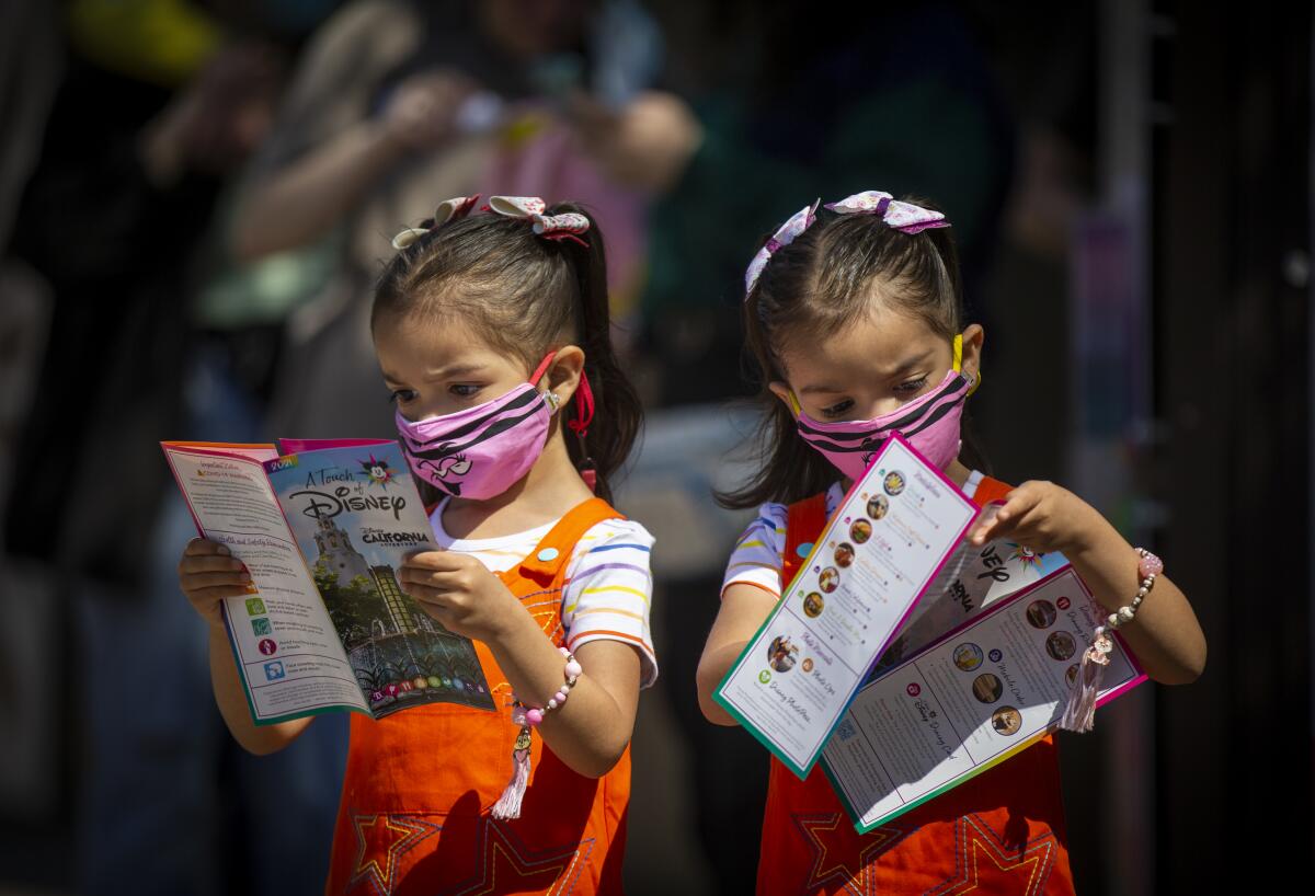 Young twin girls wearing masks look at theme park maps