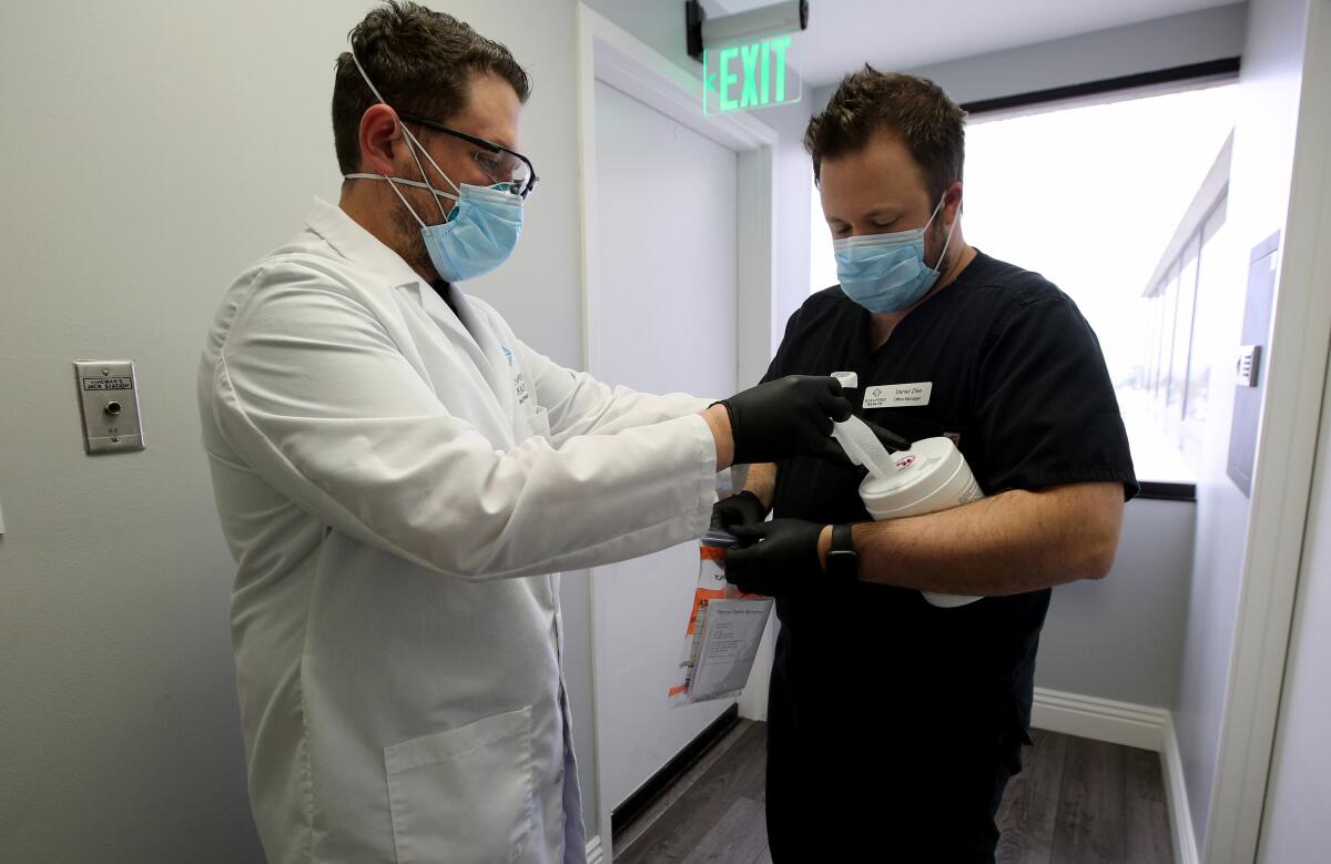 With office manager Daniel Zike lending a hand, Dr. Matthew Abinante, left , prepares to take drive-up samples to test patients for the coronavirus that causes COVID-19 outside his office in Huntington Beach.