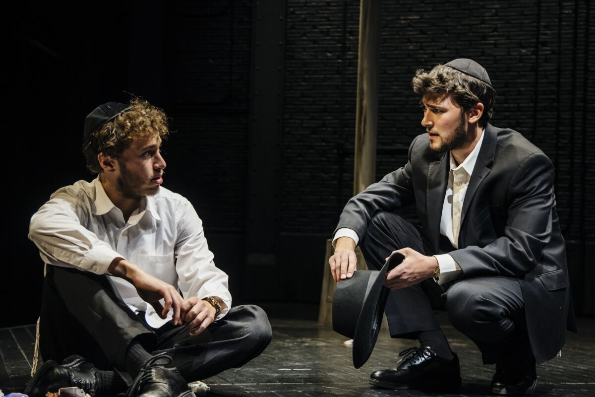 Two young men in yarmulkes sit and talk.
