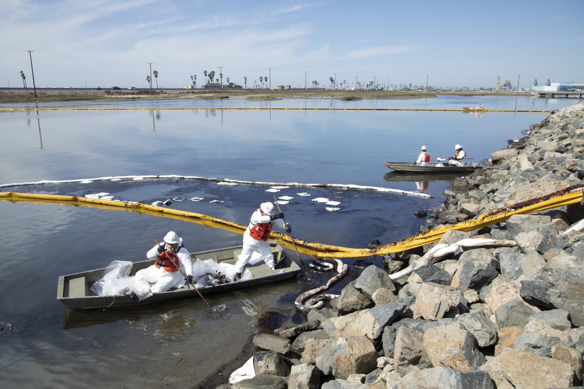Workers in boats clean up oil near a rocky shore