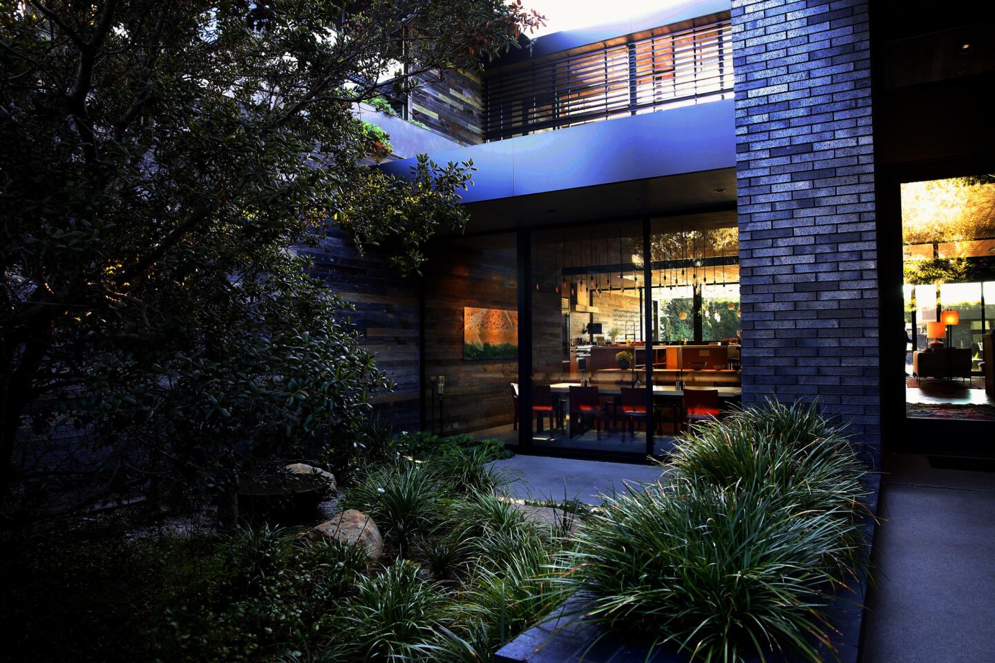 The front courtyard of the Hirsch home, designed and built by Marmol Radziner, is illuminated at dusk. Dark Iron Spot face brick and weathered wood siding unify the separate living areas.