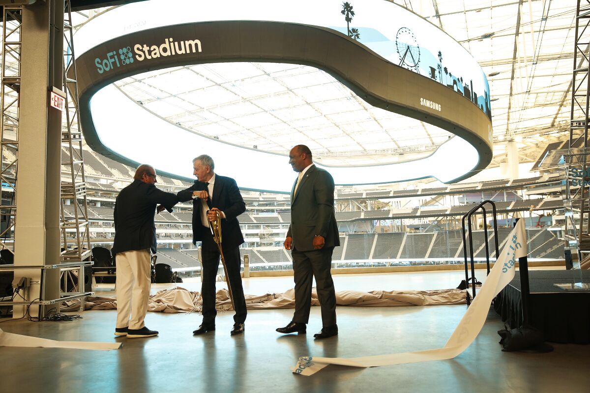 Two men bump elbows as a third watches in an empty NFL stadium.