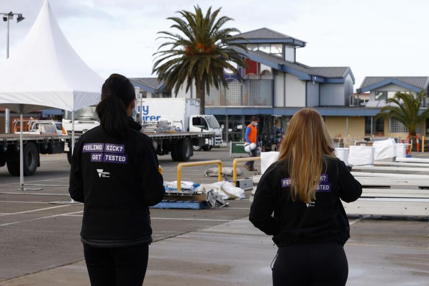 Healthcare staff watch as workers construct a pop-up COVID-19 testing site in the carpark of a college in Melbourne, Australia, Thursday, Aug. 5, 2021. Australia's second-largest city Melbourne is into its sixth lockdown with a state government leader blaming the nation's slow COVID-19 vaccination rollout for the decision. (Daniel Pockett/AAP Image via AP)