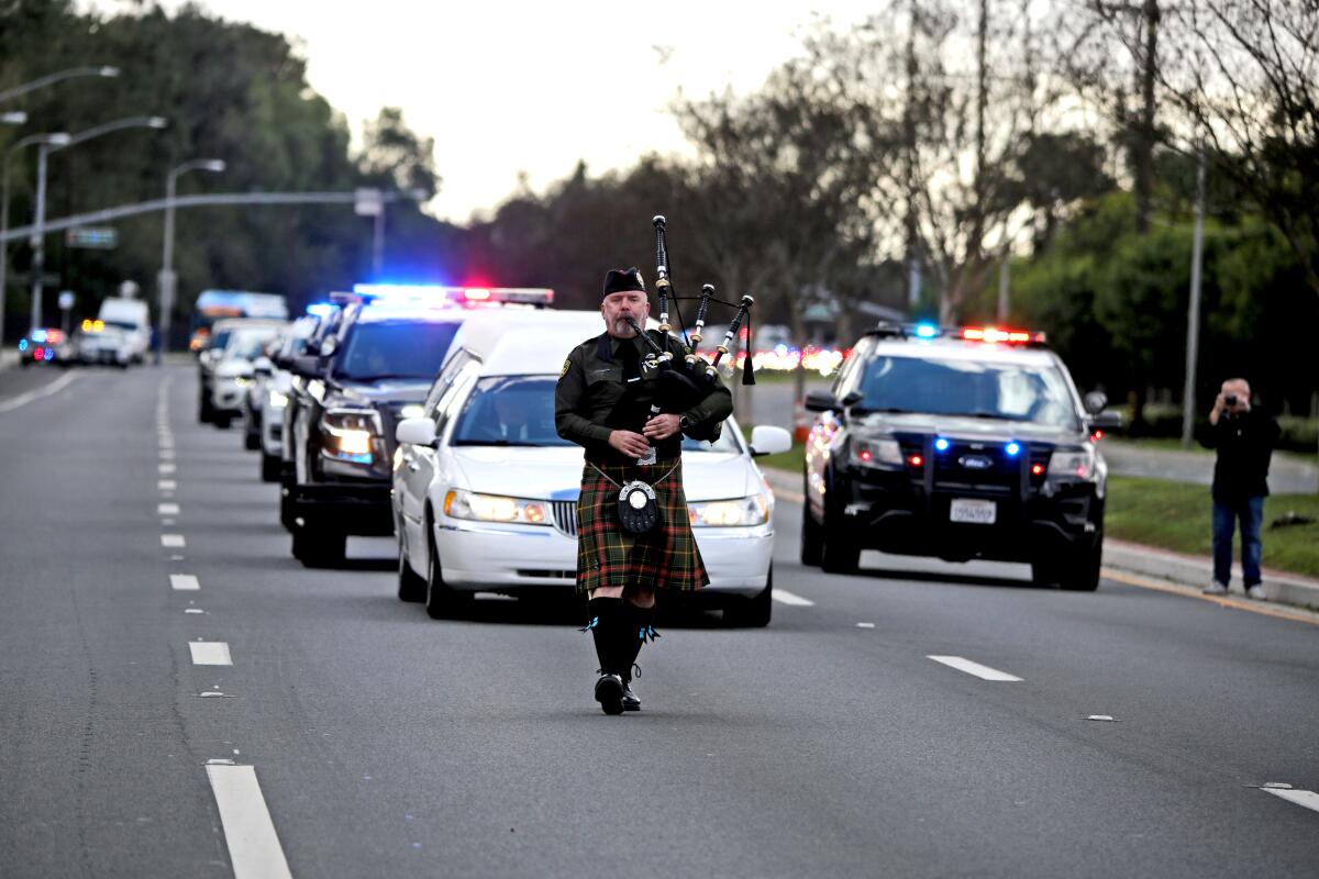 A bagpiper leads the way as a hearse carrying Huntington Beach Police Officer Nicholas Vella arrives at a funeral home.
