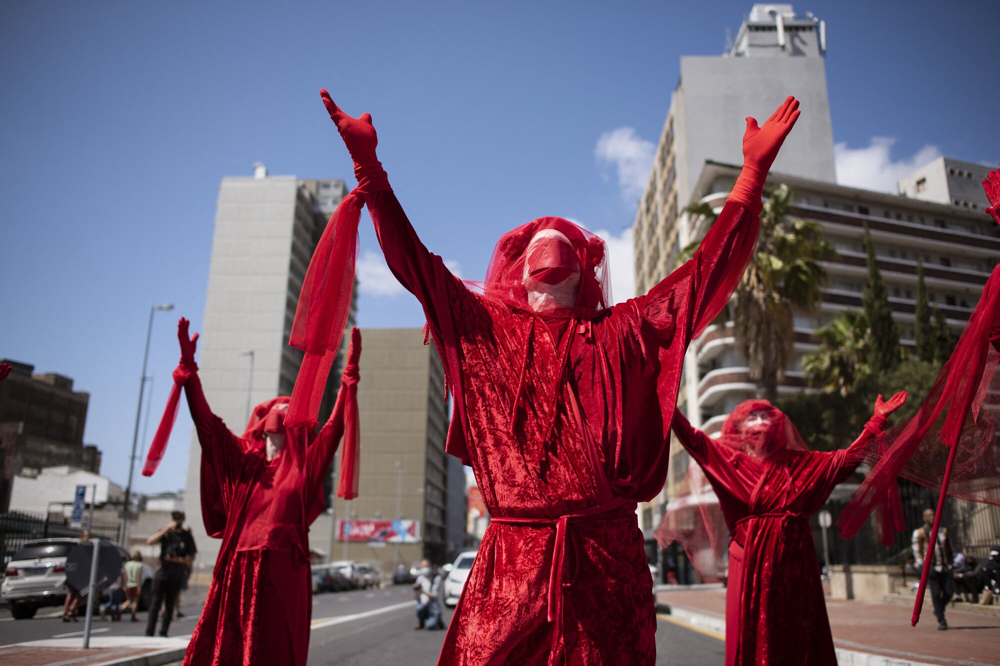 Outdoors, three people dressed in red lift their arms to the sky.