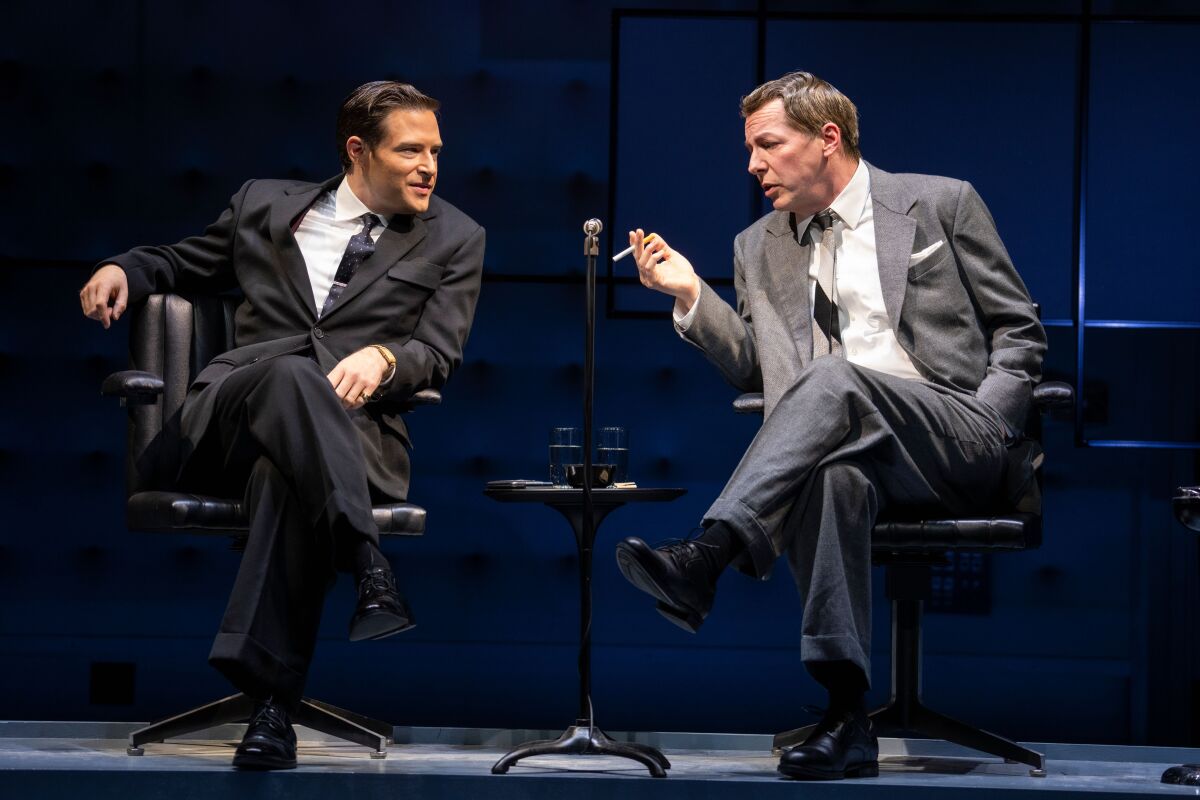 Two seated men in suits lean in to talk to each other in a scene from "Good Night, Oscar."