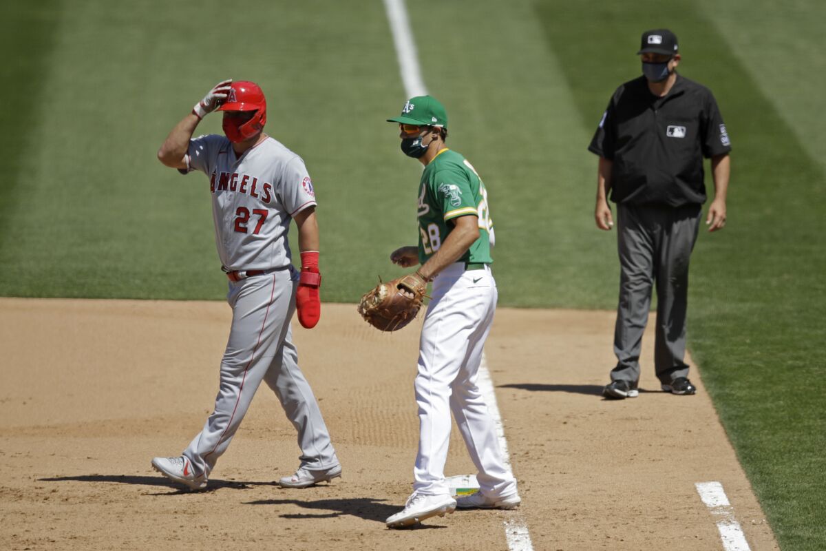 FILE - In this Monday, July 27, 2020, file photo, Oakland Athletics' Matt Olson (28) wears a mask as Los Angeles Angels' Mike Trout, left, also wears one while taking a lead off first base during the eighth inning of a baseball game in Oakland, Calif. Baseball's Western Divisions have so far avoided any COVID-related schedule disruptions and they're trying to keep it that way. (AP Photo/Ben Margot, File)