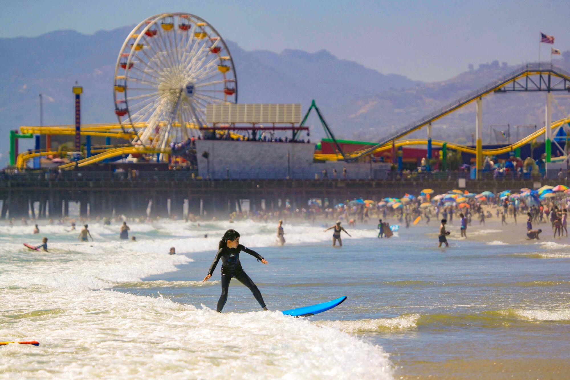 A young girl surfs in front of the Santa Monica Pier.