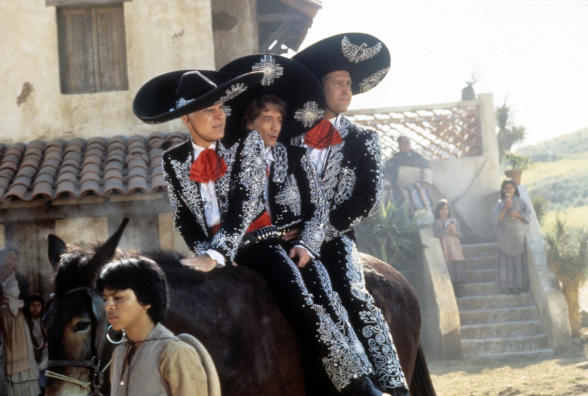 Three men dressed as mariachi performers ride a single horse in a scene from the 1986 film '¡Three Amigos!'